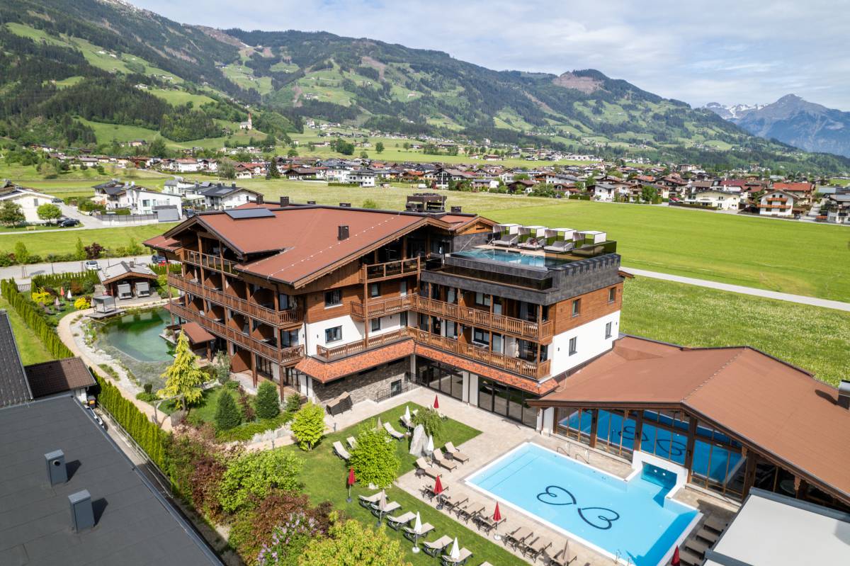 Alpenhotel mit Naturpool, Außenpool und Dachterrasse, umgeben von grüner Landschaft