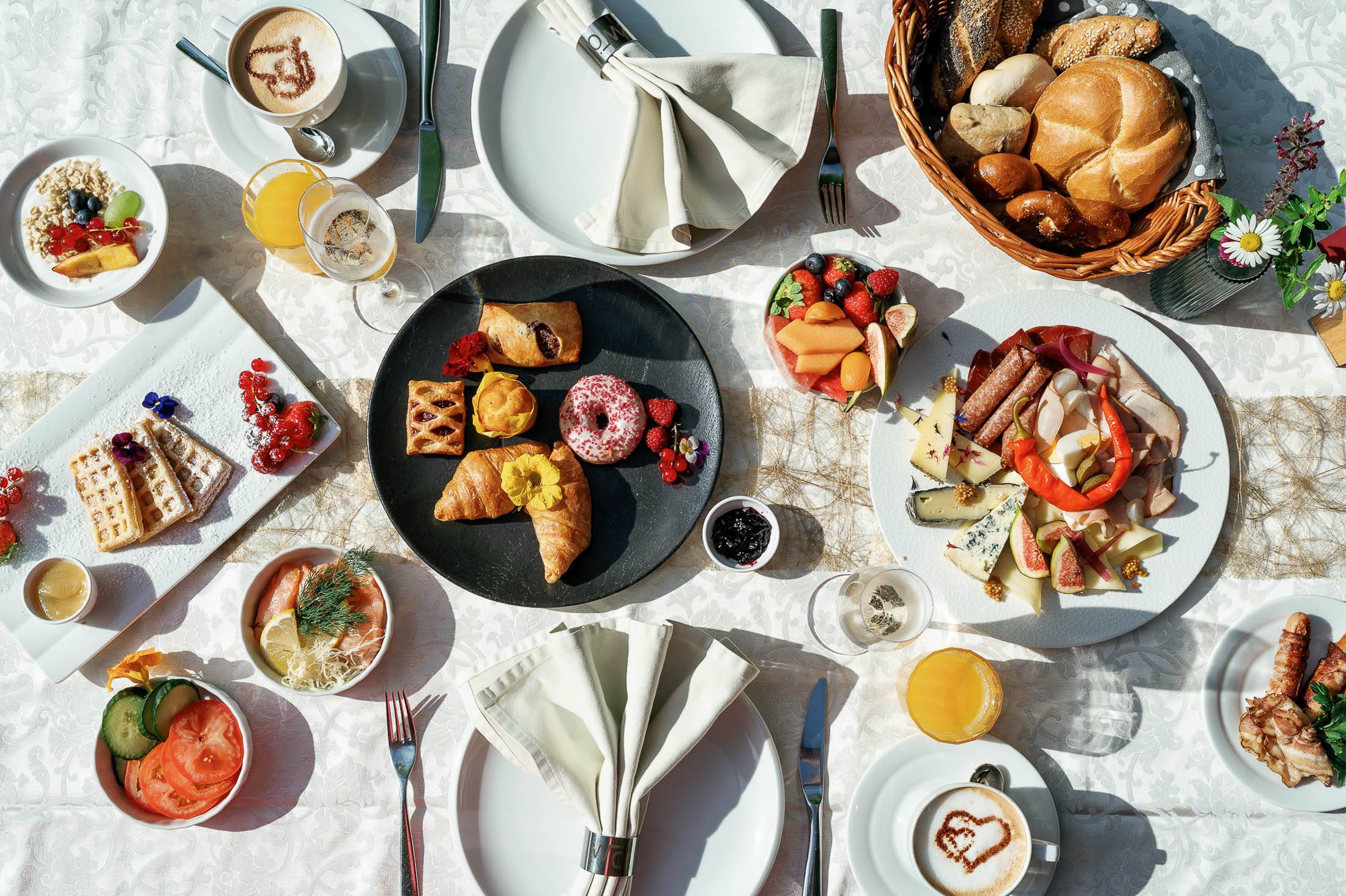 Vue de dessus d'une table de petit-déjeuner copieuse avec des gaufres, des croissants, de la charcuterie, des fruits frais, des jus et du café avec de la mousse de lait en forme de cœur