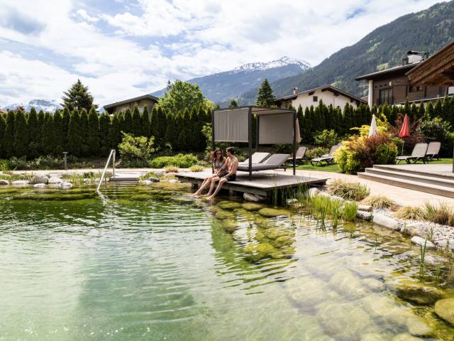 Natürlich gestalteter Badeteich mit Liegen und Pavillon, umgeben von Alpenpanorama