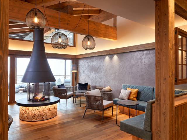 Stilvoller Lounge-Bereich mit Holzdecke und rundem Kamin inmitten bequemer Sitzgelegenheiten