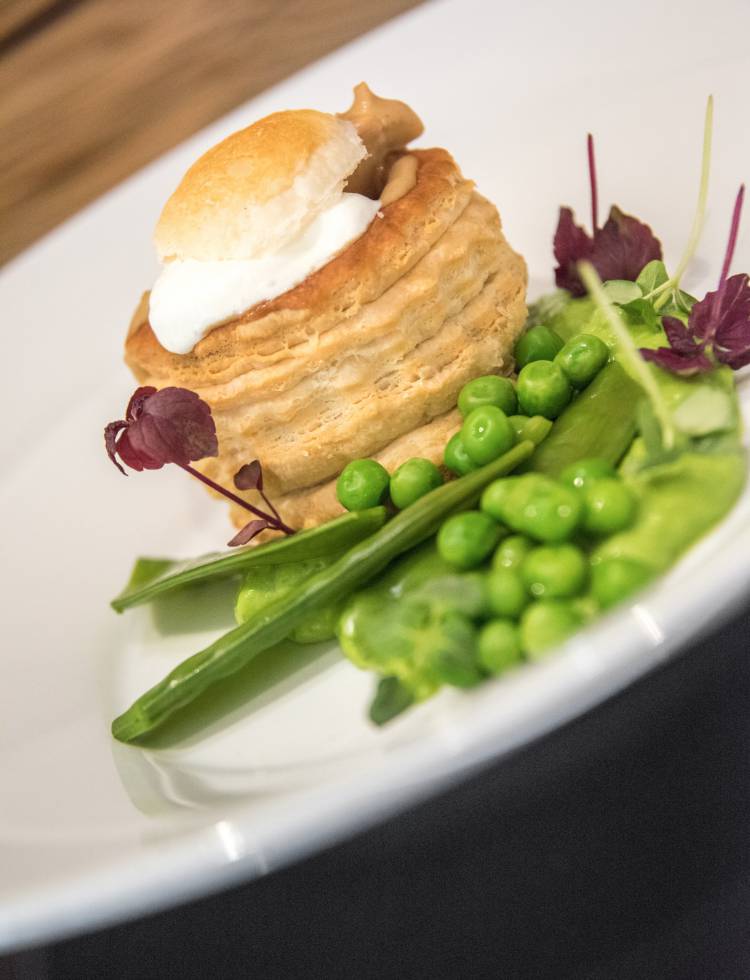 Blätterteigpastete mit pochiertem Ei, grünen Erbsen und Zuckerschoten auf weißem Teller angerichtet